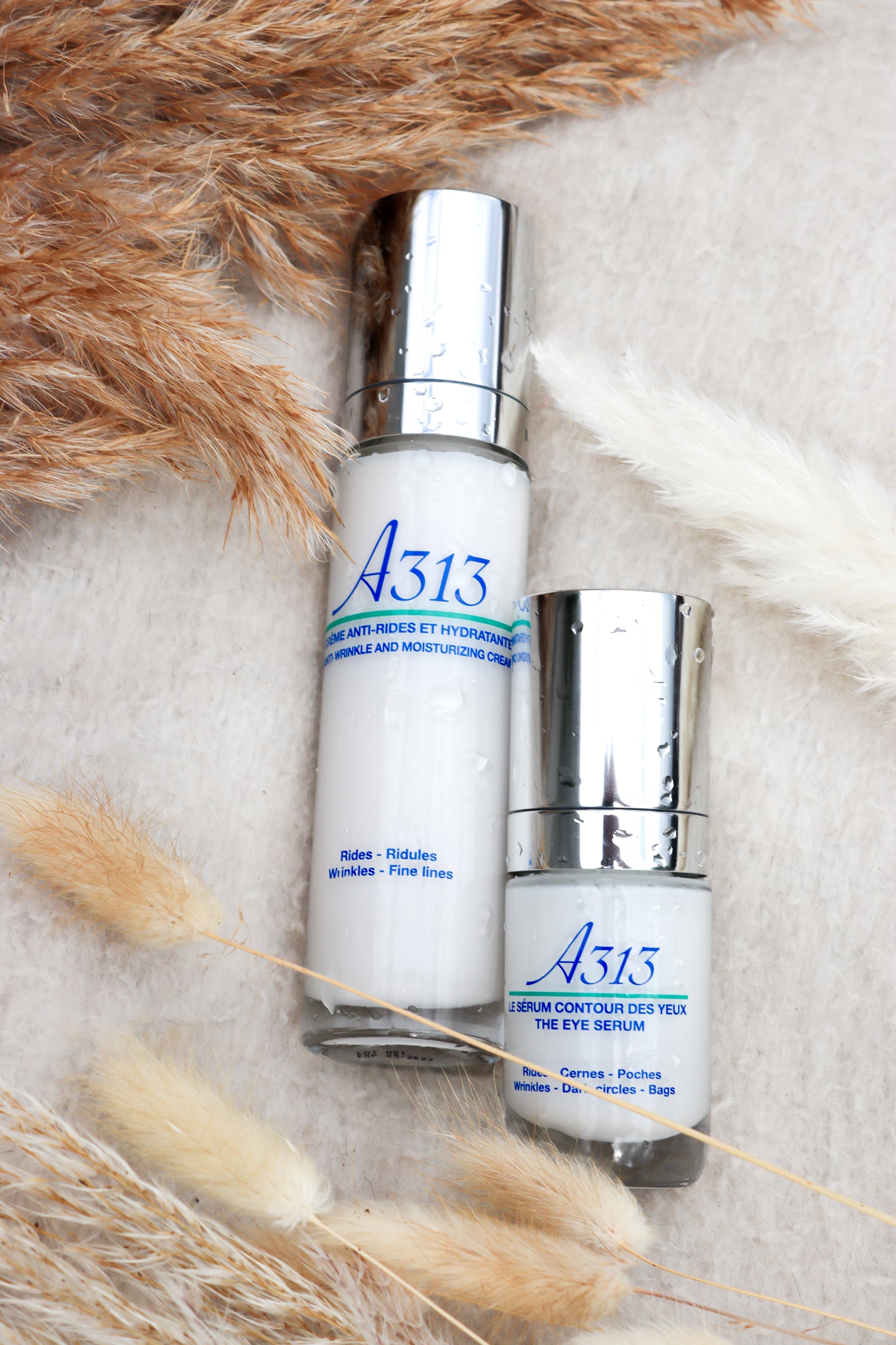 A313 wrinkle cream and eye serum bottles with silver caps on beige fabric and dried grasses