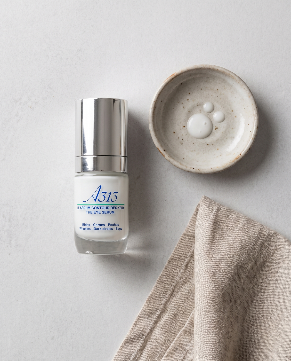 A313 Eye Serum in der Draufsicht neben einer kleinen Keramikschale und einem gefalteten Leinentuch bei weichem Tageslicht