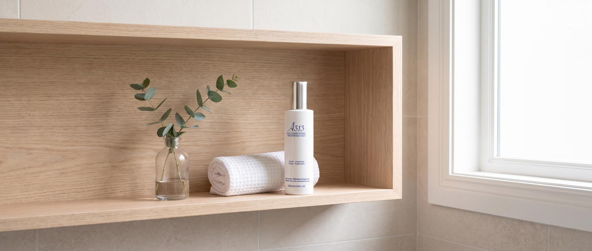 A313 Lifting Body Milk bottle on a pale-wood bathroom shelf beside a rolled white towel and a sprig of eucalyptus
