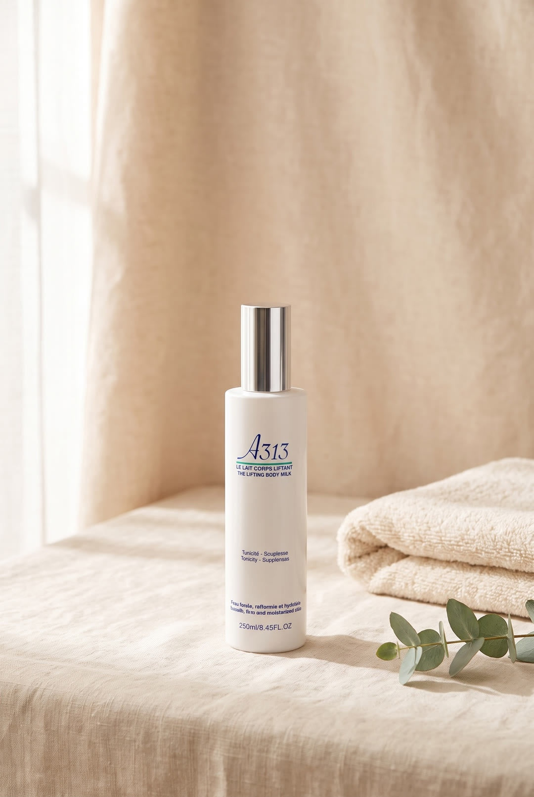 A313 Body Lifting Crème, witte fles met zilveren dop, op linnen naast een opgevouwen handdoek en eucalyptus